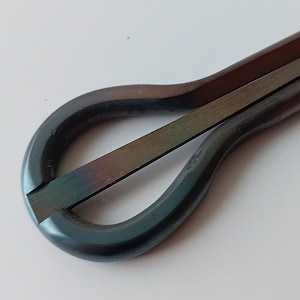 May include: A dark blue metal musical instrument called a 'thumb piano' or 'kalimba'. It has a rounded shape with a single string and a small metal loop at the end.