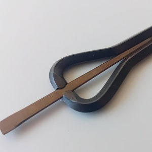 Könnte beinhalten: Ein schwarzes Metall-Musikinstrument, genannt 'Daumenklavier' oder 'Kalimba', mit einem hölzernen Resonanzboden. Das Instrument hat eine gebogene Form und eine einzige Reihe von Zinken.