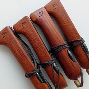 May include: Four reddish-brown wooden handles arranged diagonally, each featuring a dark cord wrapped around the center and a small bead at the end. The handles are marked with the handwritten letters F1, E1, D1, and C1 in black ink.