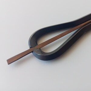 Könnte beinhalten: Ein schwarzes Musikinstrument aus Metall, genannt 'Daumenklavier' oder 'Kalimba'. Es hat eine Reihe von Metallzungen, die mit den Daumen gezupft werden, um einen Klang zu erzeugen.
