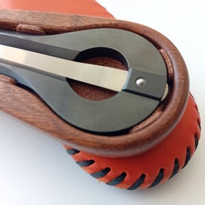 Könnte beinhalten: Ein handgehaltenes Musikinstrument aus Holz und Metall mit einer Ledertasche. Das Instrument hat einen dunklen Holzkörper und eine silberne Metallsaite.