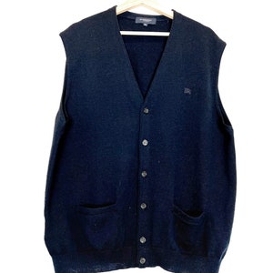 Op de afbeelding: Een zwarte, mouwloze cardigan met een knoopsluiting en twee zakken. De cardigan heeft een klein logo op de borst.