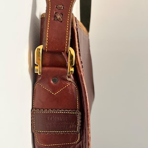 May include: A brown leather shoulder bag with a gold buckle and a yellow stitched border. The bag has a label that reads "Giovanni, Genuine Leather, Made in Italy, Torino 1483".