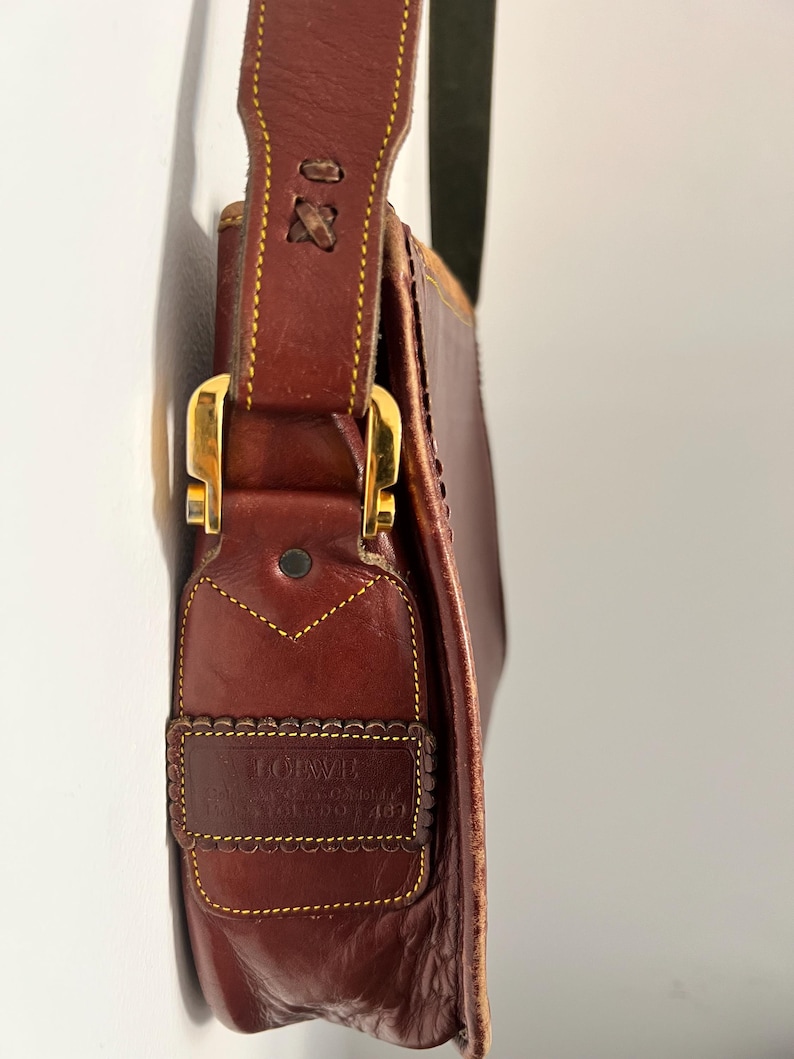 May include: A brown leather shoulder bag with a gold buckle and a yellow stitched border. The bag has a label that reads "Giovanni, Genuine Leather, Made in Italy, Torino 1483".