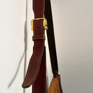 May include: A brown leather shoulder bag with a gold buckle and a brown suede strap.