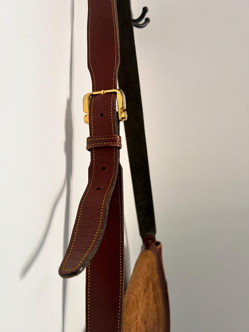 May include: A brown leather shoulder bag with a gold buckle and a brown suede strap.