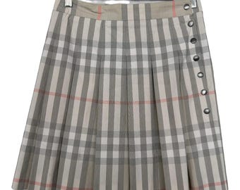 May include: A beige, gray, and pink plaid pleated skirt with a button closure. The skirt is hanging on a wooden hanger with a metal clip.
