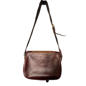 May include: A brown leather shoulder bag with a flap closure and a tassel. The bag has a brown and tan patterned fabric lining.