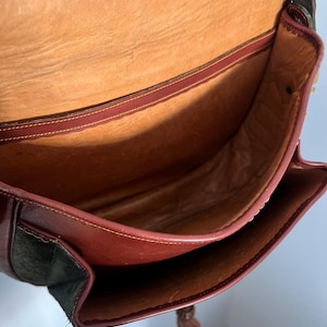 May include: The inside of a brown leather bag with a suede bottom. The bag has a brown leather flap and a tassel.