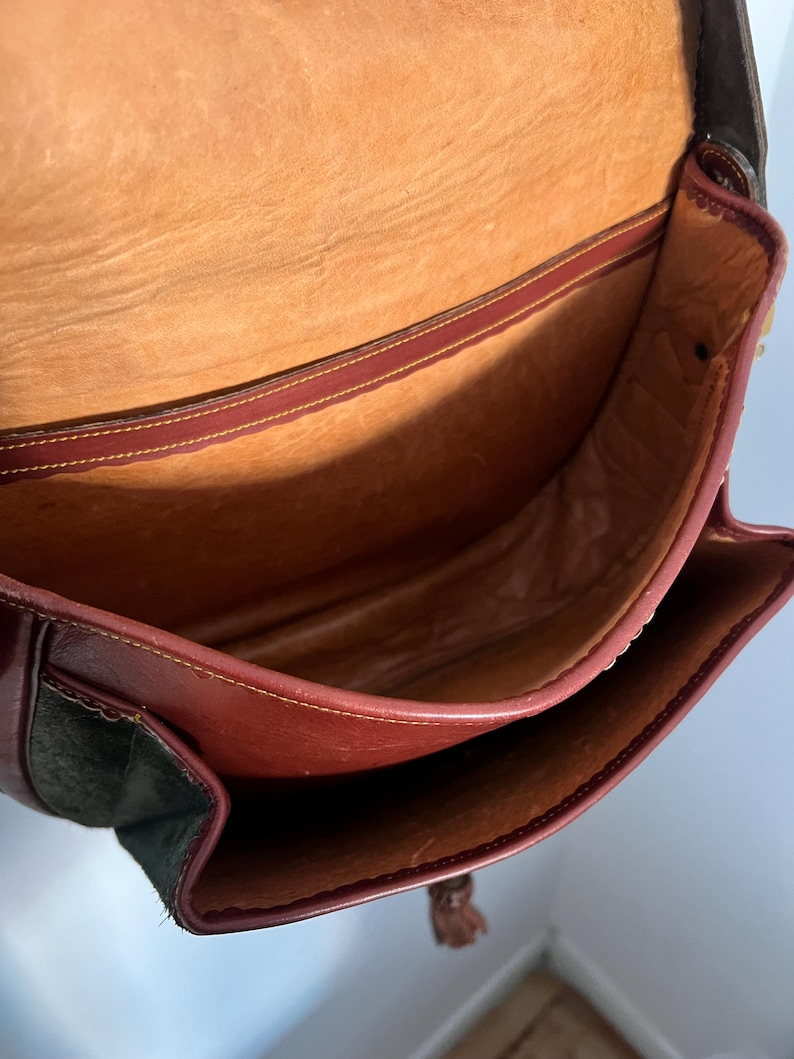 May include: The inside of a brown leather bag with a suede bottom. The bag has a brown leather flap and a tassel.