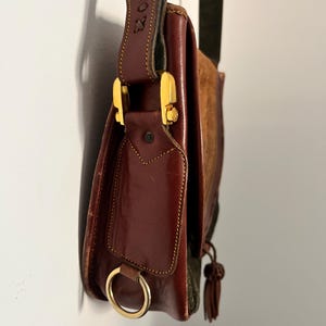 May include: A brown leather shoulder bag with a gold buckle and a tassel. The bag has a flap with a small pocket and a ring on the side.