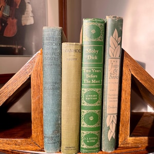 May include: A collection of antique books displayed on a wooden shelf. The books have various colors and titles, including "Brief History of the United States" and "Moby Dick." The shelf is part of a corner unit.