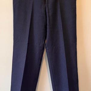 May include: Navy blue dress pants with vertical pinstripes. The pants are hanging on a black hanger. The pants have a classic, tailored design, suitable for formal or business attire.