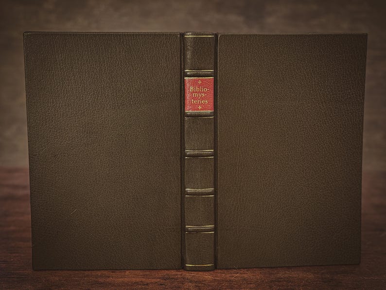 Puede incluir: Un libro antiguo cerrado, con una cubierta de cuero marr&oacute;n oscuro. El lomo, en un color contrastante, presenta el t&iacute;tulo "Bibliomysteries" en rojo. La imagen destaca el cuero texturizado y el dise&ntilde;o cl&aacute;sico del libro.