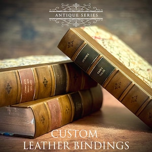 May include: Three antique-style leather-bound books stacked on a wooden surface. The top book has the title "Grimm's Fairy Tales" on the spine. The middle book has the title "Complete Sherlock Holmes" on the spine. The bottom book has a title that is partially obscured. The text "CUSTOM LEATHER BINDINGS" is printed below the books.