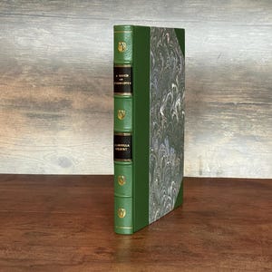 Puede incluir: Un libro de tapa dura con lomo verde y cubierta jaspeada. El lomo presenta letras doradas y elementos decorativos. El t&iacute;tulo del libro, "A Touch of Eternity" y el autor, "Isabella Gilbert" son visibles.