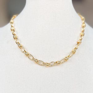 Peut inclure: Un collier en chaîne dorée avec un design délicat de maillons torsadés. Le collier est présenté sur un buste de mannequin blanc.
