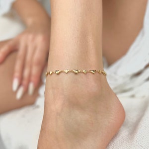 Peut inclure: Un bracelet de cheville en or avec une chaîne délicate et de petits pendentifs en forme de cœur.