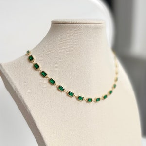 May include: A gold chain necklace with emerald green rectangular stones.