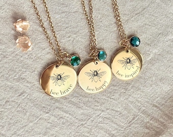 May include: Three gold necklaces with bee charms and green gemstone accents. Each charm has a different inscription: "bee brave", "bee happy", and "bee inspired".