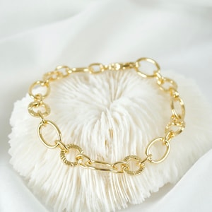 May include: A gold chain bracelet with oval links. The links have a textured design.