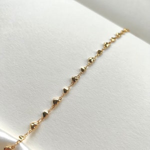Peut inclure: Un bracelet en chaîne dorée avec de petits pendentifs en forme de cœur.