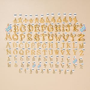 K&ouml;nnte beinhalten: Eine Sammlung von goldfarbenen Metallanh&auml;ngern in Reihen, bestehend aus Tierkreiszeichen, Buchstaben im Bubble-Stil mit klaren Steinen, Standard-Serifen-Alphabetbuchstaben sowie mit Strasssteinen besetzten Buchstaben und Zahlen, jeweils nummeriert.