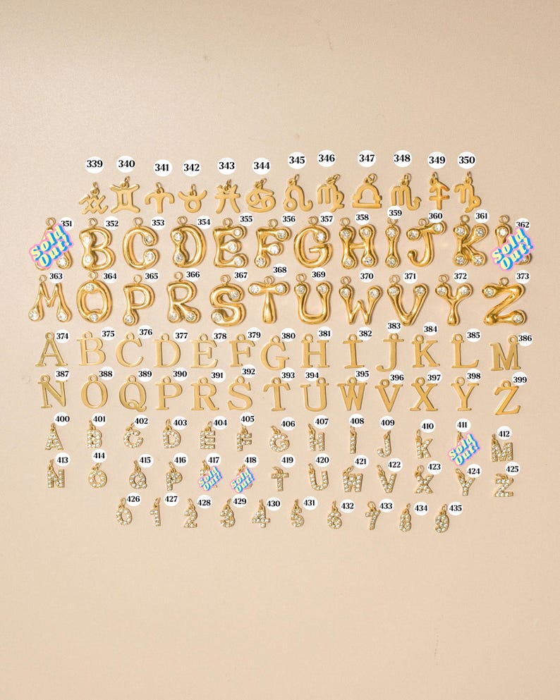 K&ouml;nnte beinhalten: Eine Sammlung von goldfarbenen Metallanh&auml;ngern in Reihen, bestehend aus Tierkreiszeichen, Buchstaben im Bubble-Stil mit klaren Steinen, Standard-Serifen-Alphabetbuchstaben sowie mit Strasssteinen besetzten Buchstaben und Zahlen, jeweils nummeriert.