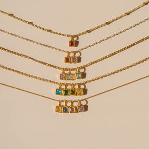 以下が含まれることがあります： カラフルな正方形のペンダントが付いたゴールドトーンのネックレス。各ネックレスは、繊細なチェーンと、赤、青、緑、黄色など、さまざまな色の複数の宝石が付いたペンダントが特徴です。ペンダントはクラスター状に配置されています。