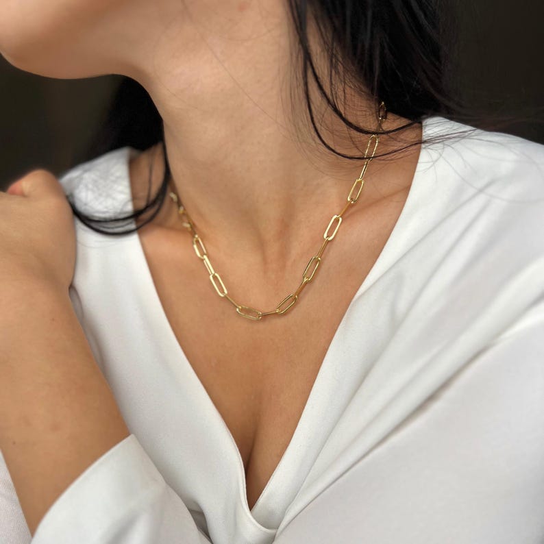 K&ouml;nnte beinhalten: Eine goldene Kettenkette mit einem einfachen, verlinkten Design. Die Kette besteht aus kleinen, ovalen Gliedern.