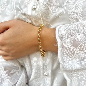 Könnte beinhalten: Ein goldenes Kettenarmband mit runden Gliedern. Das Armband befindet sich an einem Handgelenk.
