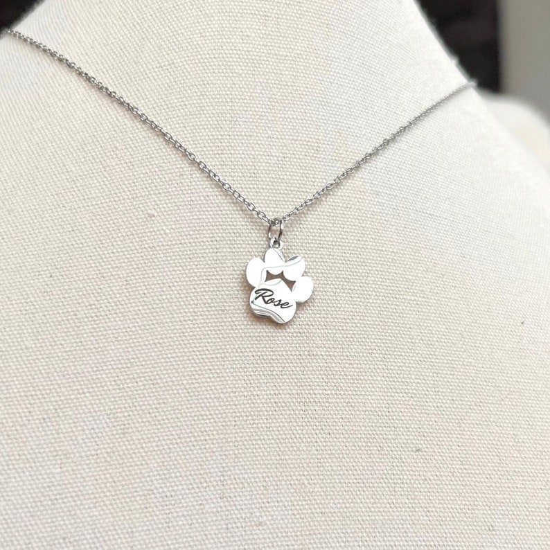 May include: Silver necklace with a paw print charm that says "Rose" on it.