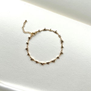 May include: A gold heart-shaped charm bracelet with a delicate chain. The bracelet is made of metal and has a lobster clasp closure.