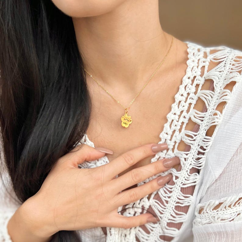 May include: A gold chain necklace with a small gold paw print pendant. The pendant has the word "Lola" engraved on it.