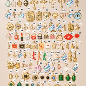 K&ouml;nnte beinhalten: Eine Sammlung verschiedener Metallanh&auml;nger, nummeriert von 86 bis 182, mit verschiedenen Formen wie Kreuzen, Augen, Herzen, Handtaschen, Spielkarten, Tieren und geometrischen Steinen. Einige Anh&auml;nger sind mit dem Text Sold Out in Blau und Pink markiert.