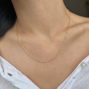 May include: A gold chain necklace with a delicate rope design. The necklace is worn by a person with a white shirt.