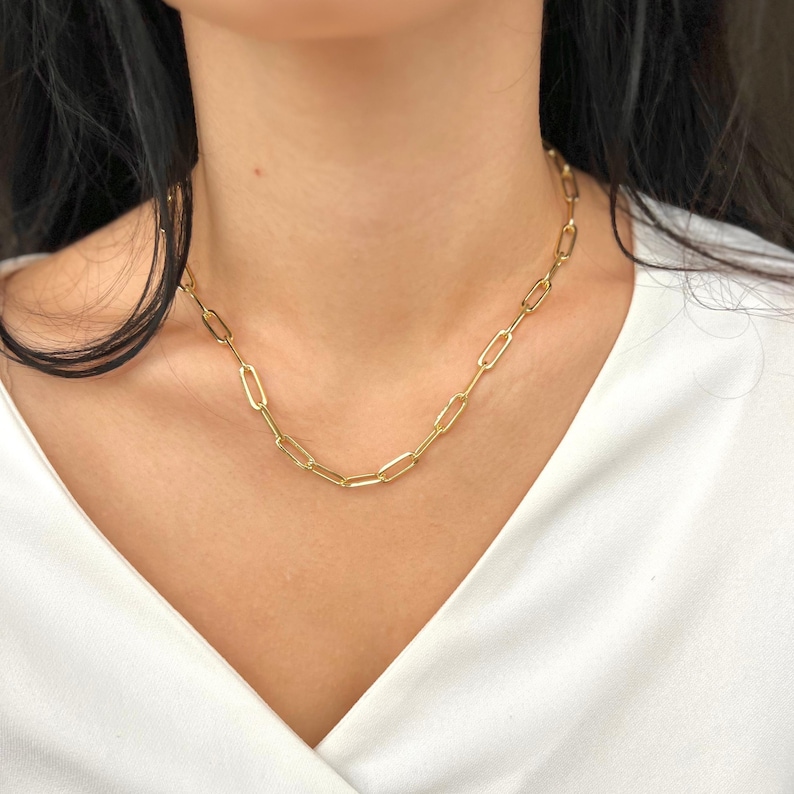 K&ouml;nnte beinhalten: Eine goldene Kettenkette mit einem einfachen, verlinkten Design. Die Kette besteht aus kleinen, ovalen Gliedern.