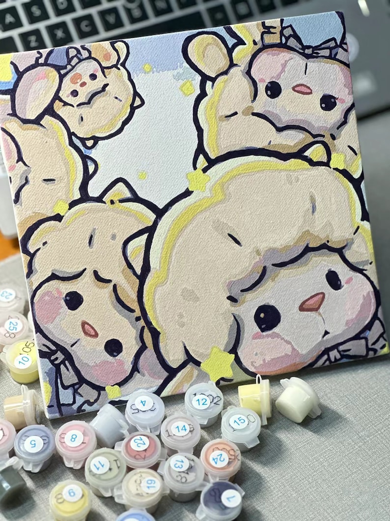 May include: A paint by numbers kit with a canvas featuring a cartoon illustration of three fluffy white sheep with pink cheeks and black eyes. The canvas is surrounded by small plastic containers of paint with numbers on the lids.