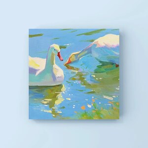 May include: Two white geese swimming in a blue pond with green grass and yellow flowers. The geese are facing each other, with one looking directly at the viewer.