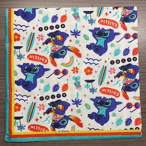 Puede incluir: Servilletas de papel blancas con un patr&oacute;n repetido de Stitch de Lilo & Stitch. Stitch se representa en varias poses, incluyendo tocando el ukelele, haciendo surf y pasando el rato. El fondo presenta palmeras, flores y las palabras "Aloha" y "Chillin'." Las servilletas tienen un borde rojo, amarillo y azul.