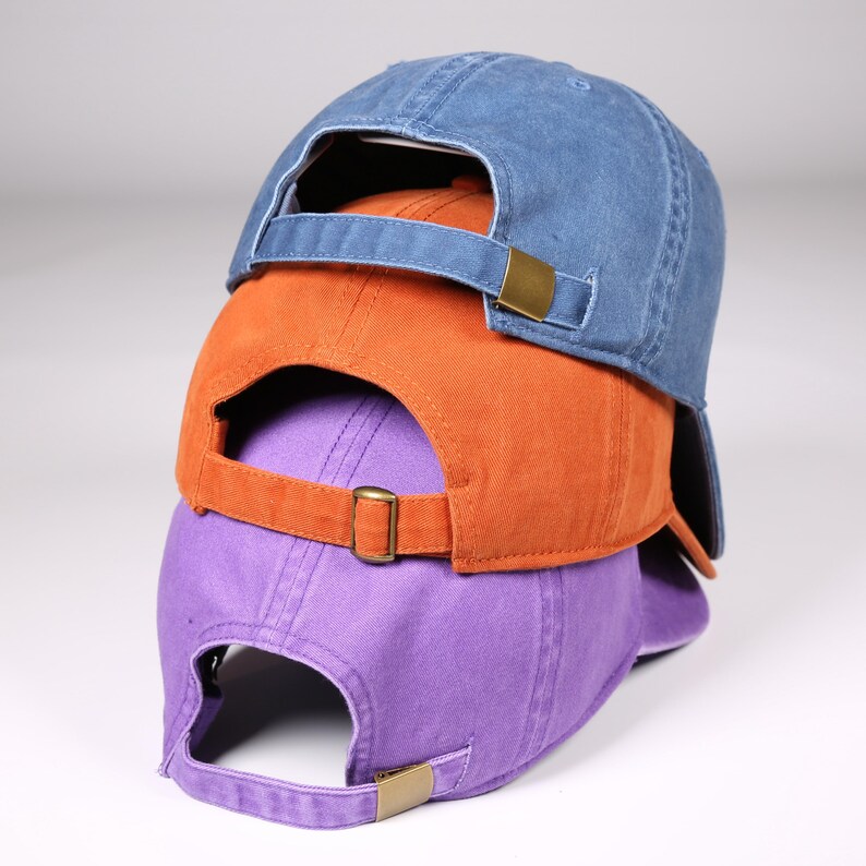 May include: Three baseball caps stacked on top of each other. The top cap is blue, the middle cap is orange, and the bottom cap is purple. Each cap has a curved brim and an adjustable strap with a metal buckle.