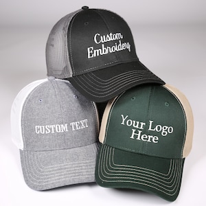 May include: Three baseball caps with mesh backs. One is black with "Custom Embroidery" in white, another is gray with "Custom Text", and the third is green with "Your Logo Here". All have curved visors.