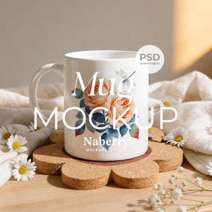 May include: White ceramic mug featuring a floral design with peach roses and blue leaves, and a dragonfly. The mug is on a cork coaster and surrounded by daisies and a white cloth. Text on the mug reads "Mug Mockup" and "Naberry Mockups Studio."