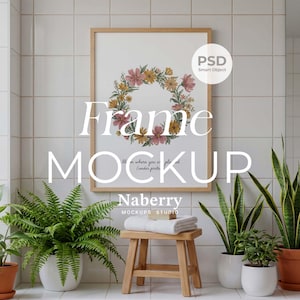 May include: A framed floral wreath print with the text "Frame MOCKUP" hangs on a white tiled wall. A wooden stool holds a folded white towel. Potted plants in white and terracotta pots are arranged around the stool.