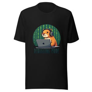 Op de afbeelding: Een zwart t-shirt met korte mouwen en een afbeelding van een bruine hamster met een koptelefoon op achter een laptop. De achtergrond is een groene cirkel vol binaire code. Onder de hamster staat de tekst DEBUGGING MODE in het groen.