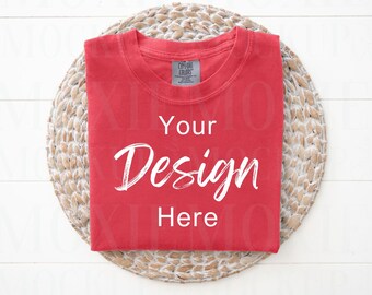 May include: Red t-shirt folded on a woven placemat. The t-shirt has the text "Your Design Here" printed on it.