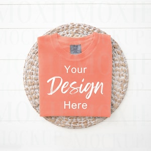May include: A coral colored t-shirt with a white background and the text "Your Design Here" on a woven straw placemat.