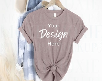 May include: A mauve coloured t-shirt with short sleeves hanging on a wooden hanger. The t-shirt has the text "Your Design Here" printed on the front.