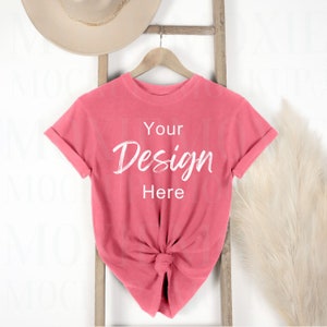 May include: A coral pink t-shirt with rolled up sleeves is hanging on a wooden ladder. The t-shirt has the text "Your Design Here" written on the front in white.