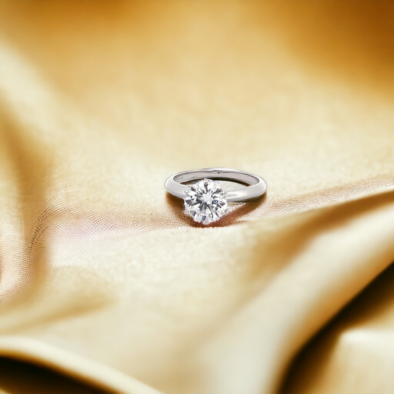May include: A silver ring with a large, round, clear diamond set in the center.